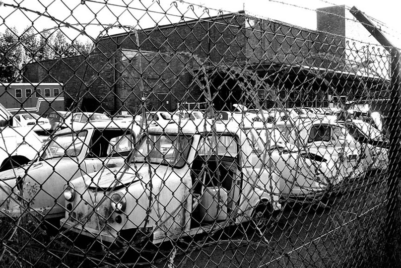 Rows of derelict invalid carriages seen behind a chain-link fence.